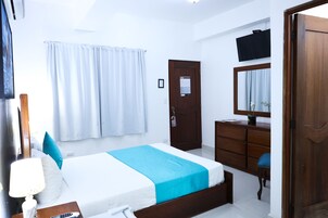 A hotel room with a bed, a desk, a chair, a dresser, and a television on the wall.