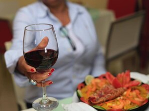 Une personne tenant un verre de vin, avec une assiette de nourriture en arrière-plan.