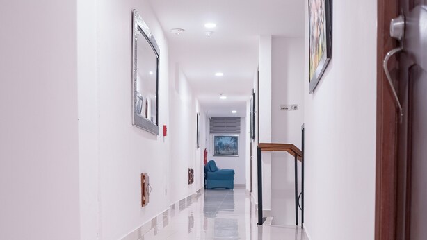A clean, well-lit hallway with a polished floor, a blue sofa in the distance, and a door with a handle on the right. - Cataleya Hotel (Santo Domingo)
