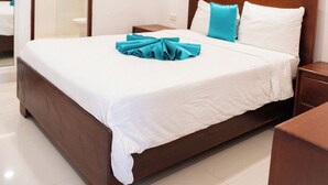 Une chambre d’hôtel avec un grand lit, une tête de lit en bois, une table de chevet et une salle de bain visible à travers une porte ouverte.