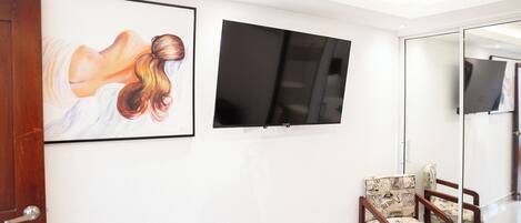 Una habitación moderna con un televisor de pantalla plana en la pared, una obra de arte enmarcada y dos sillones estampados.
