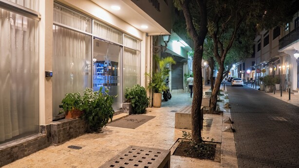 L’entrée d’un hôtel, avec une porte en verre, des plantes en pot et un trottoir pavé.