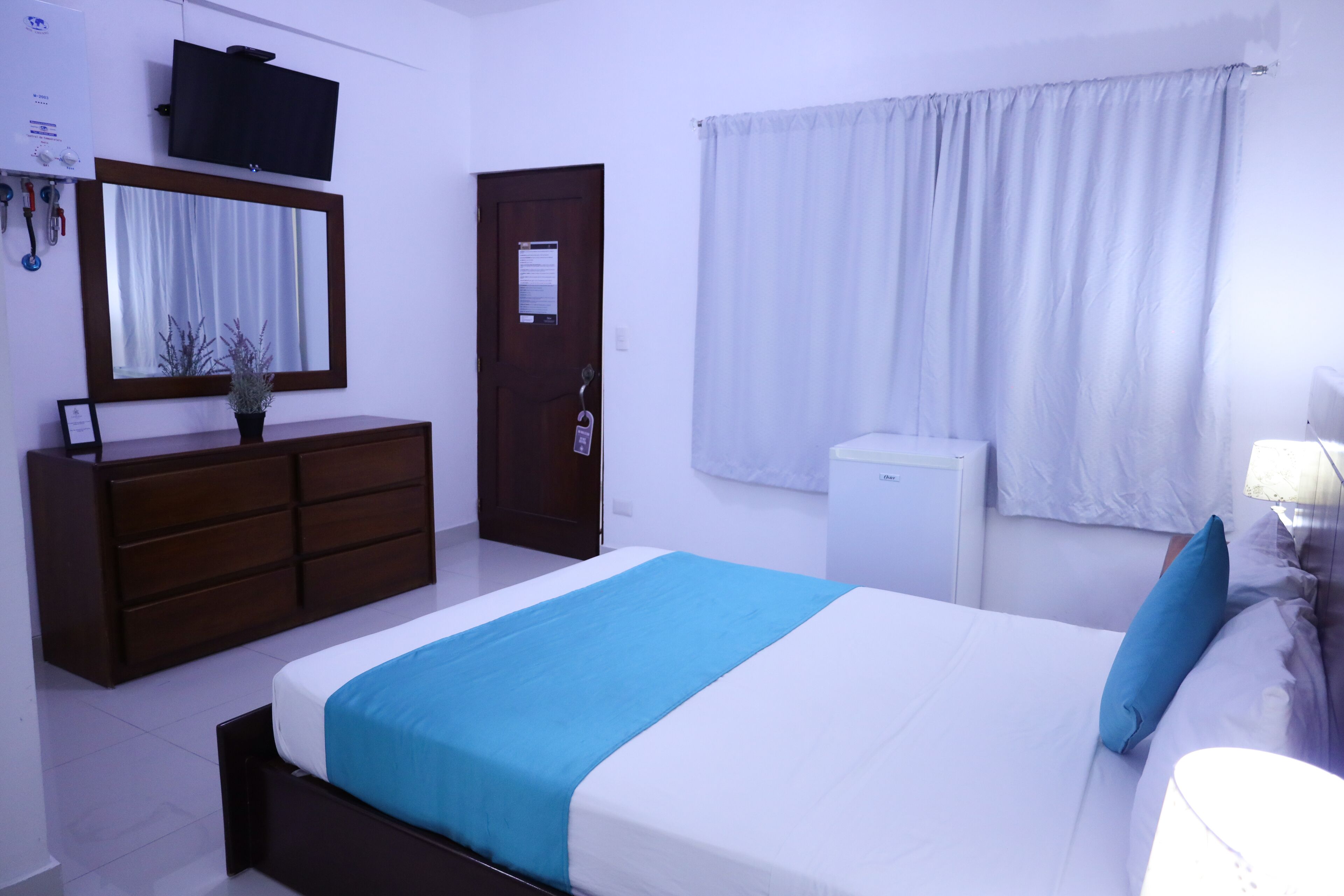 A hotel room with a bed, a dresser, a mirror, a television, and a window with curtains.