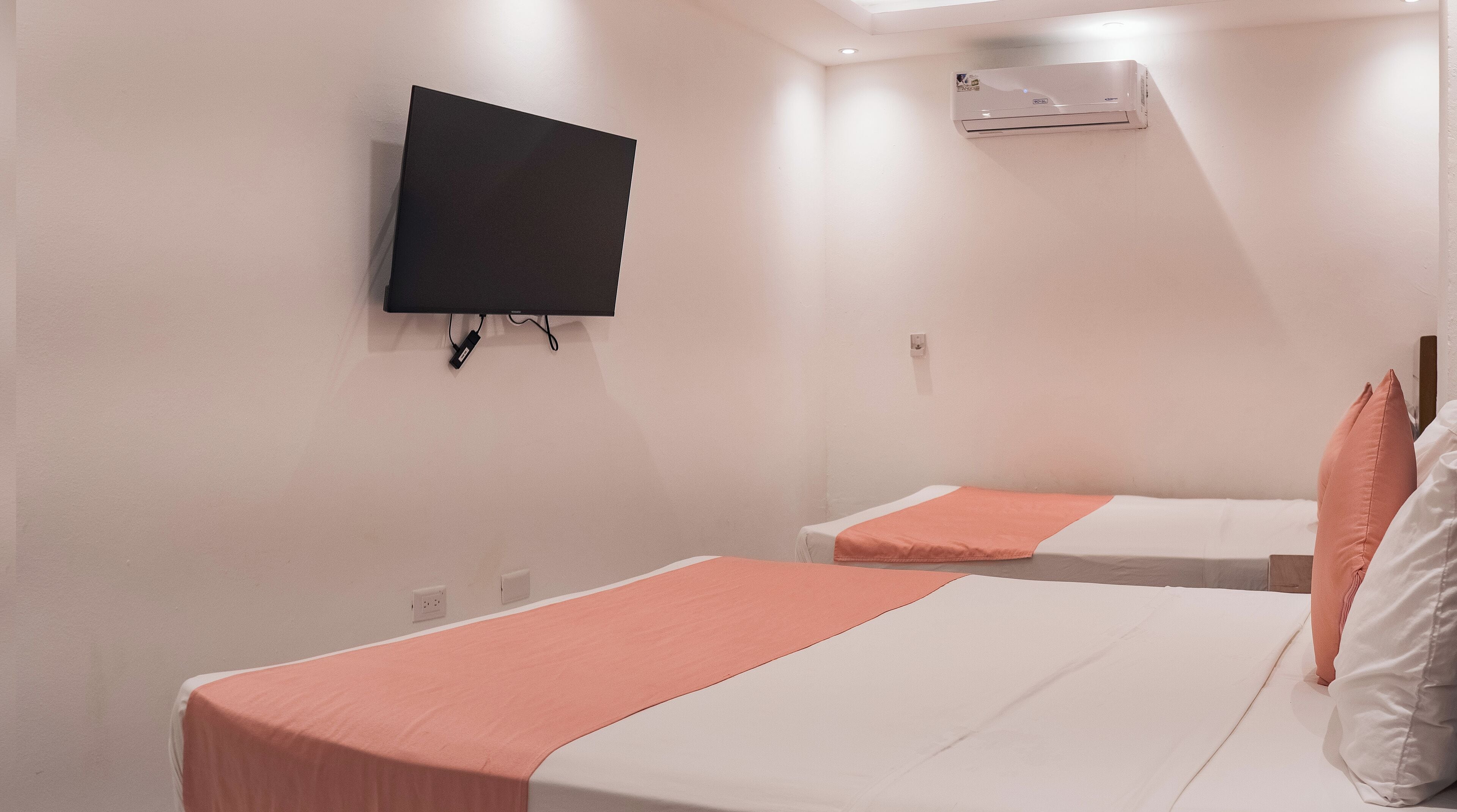A hotel room with two beds, a TV mounted on the wall, and an air conditioning unit.