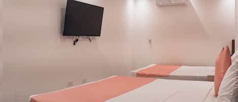A hotel room with two beds, a TV mounted on the wall, and an air conditioning unit.
