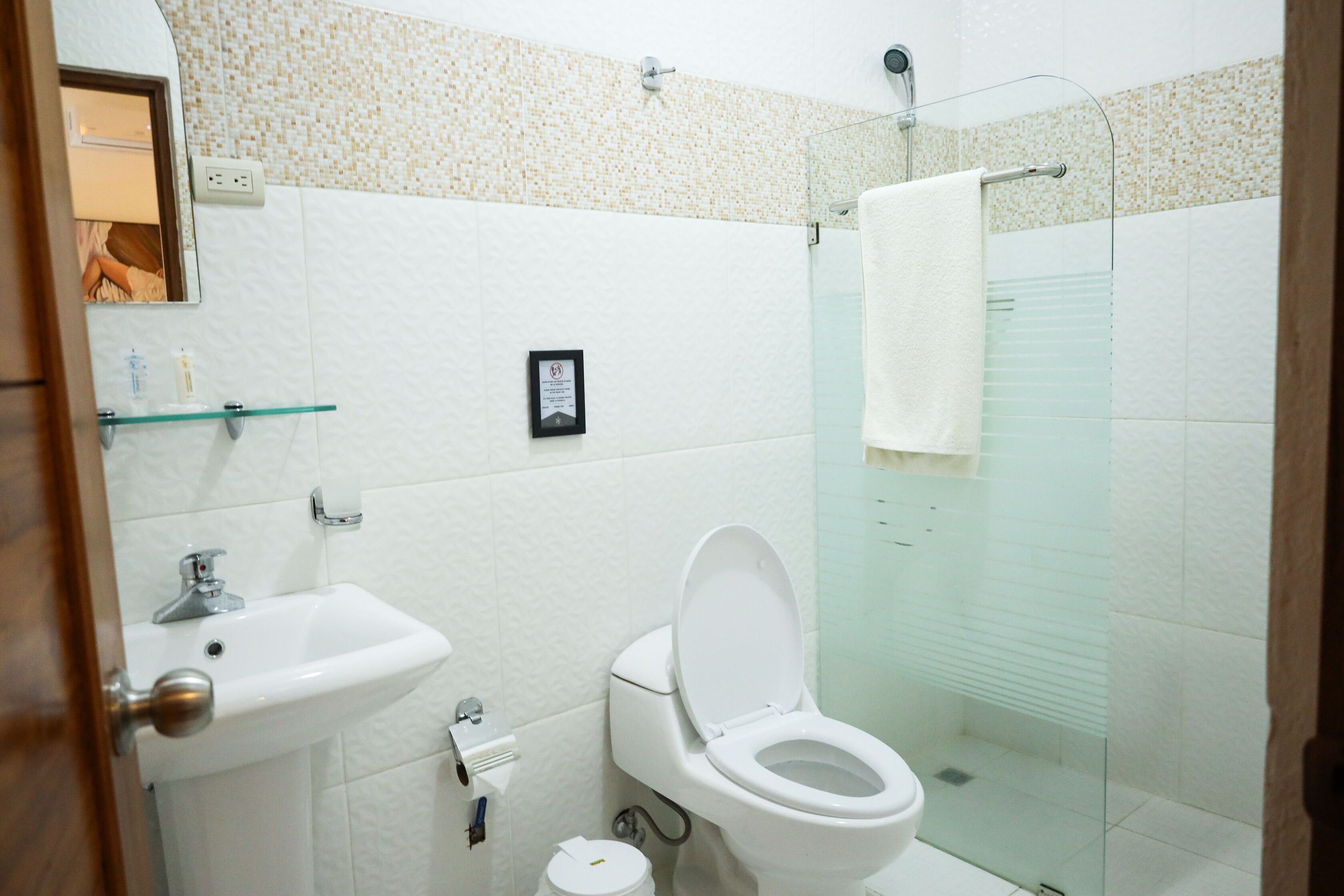 Et badeværelse med et hvidt håndvaskarrangement, toilet og glasbrusekabine.