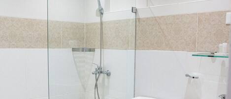A modern bathroom with a glass-enclosed shower, a toilet, a sink, and a trash bin.