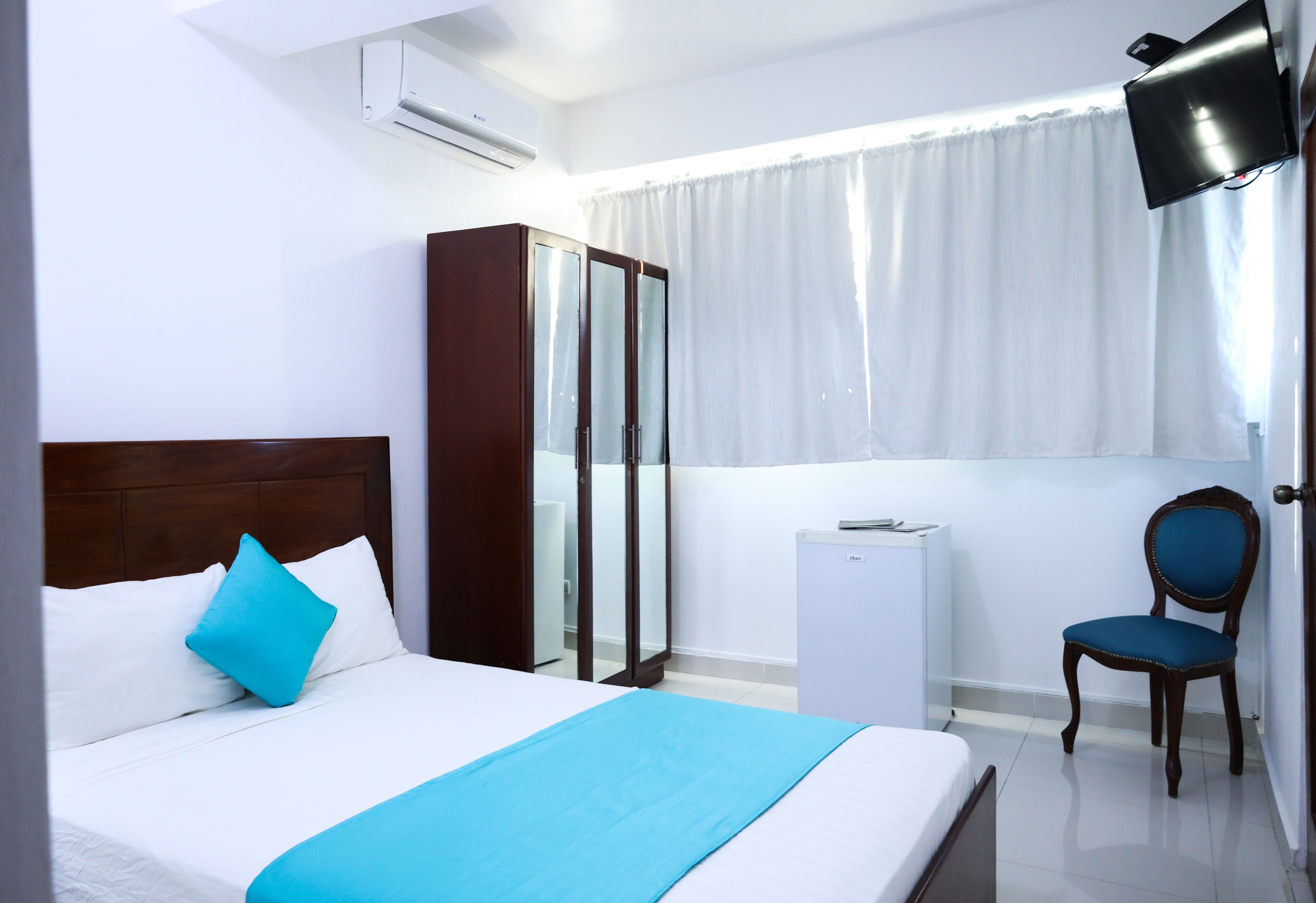 A hotel room with a bed, a wardrobe, a chair, and a TV mounted on the wall.