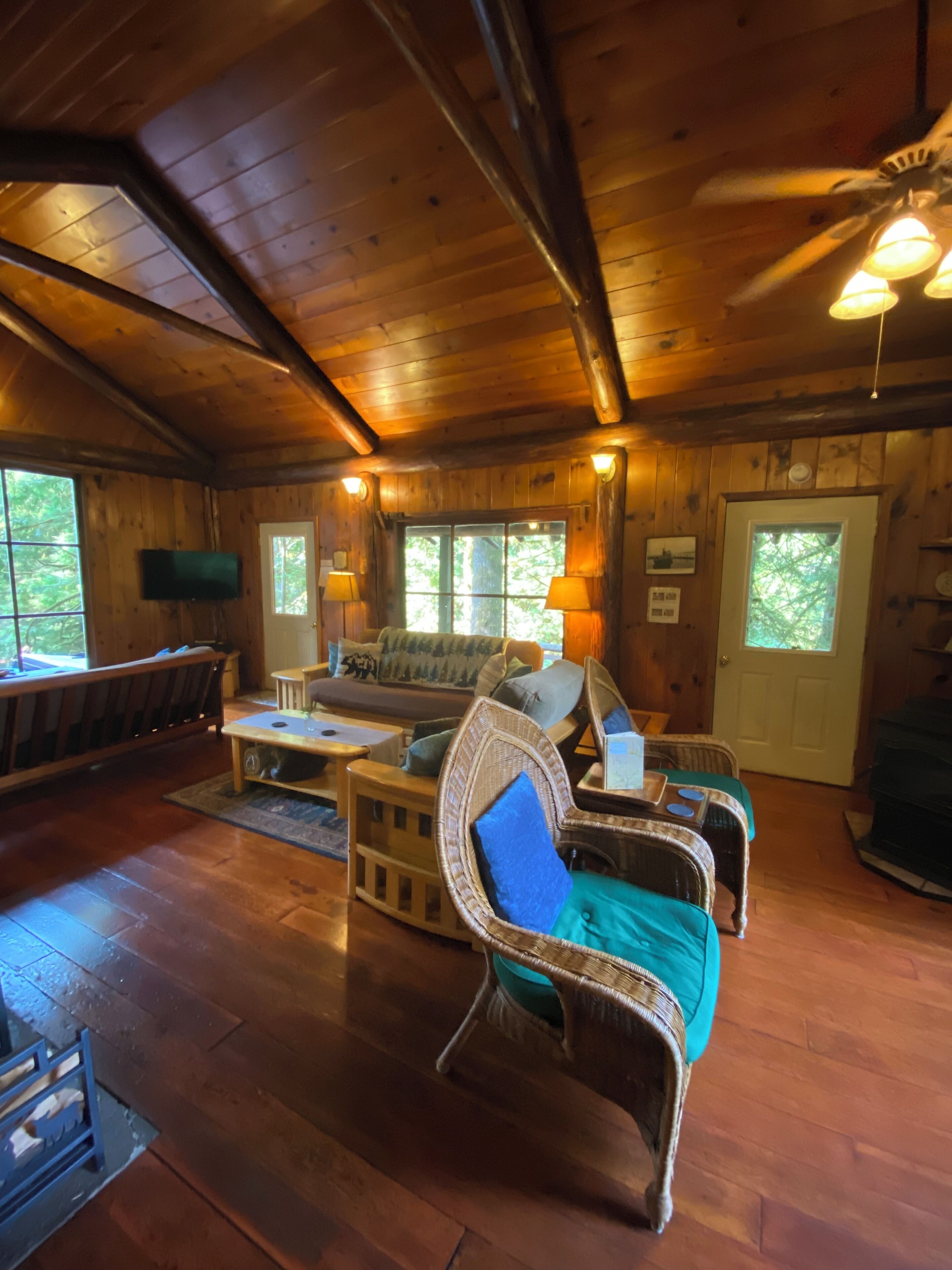 L’intérieur chaleureux d’un chalet avec des murs en bois, un ventilateur de plafond, un canapé et un téléviseur fixé au mur.