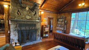 Interior acogedor de una cabaña con chimenea de piedra, muebles de madera y una estantería.