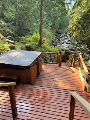 A wooden deck with a hot tub and a view of a forested area with a stream. - Total Seclusion, 50 Private Acres, 2000 Ft Riverfront, Mountain Cabin, Hot Tub (Baring)