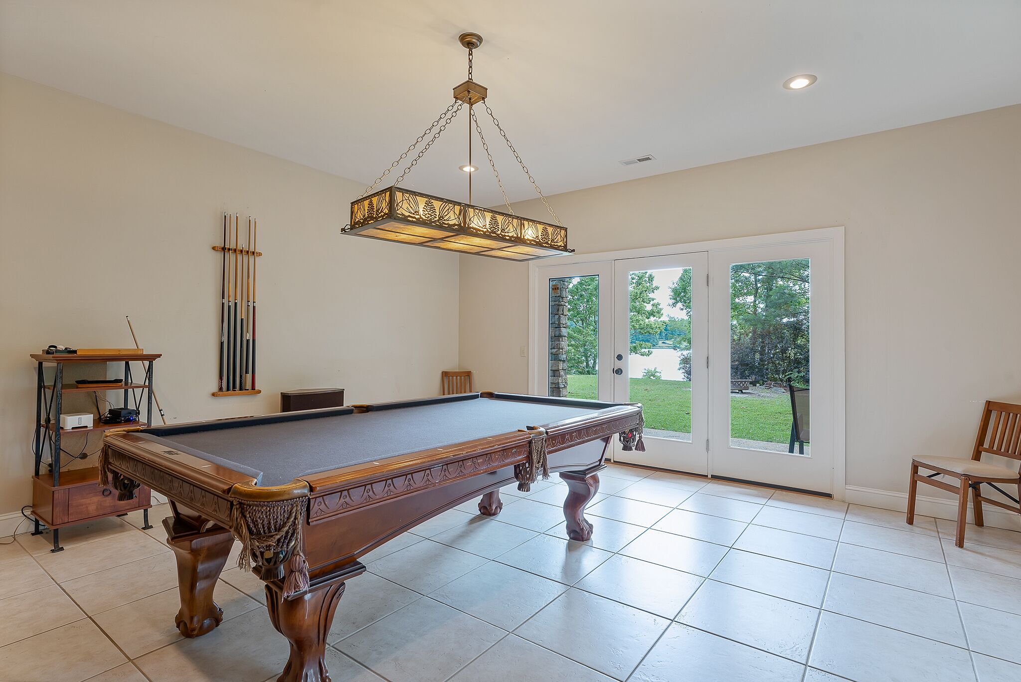 A pool table with a hanging light fixture, a billiard rack, and a chair.
