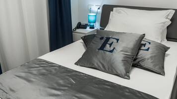 A neatly made bed with a grey bedspread and two pillows with embroidered letters.
