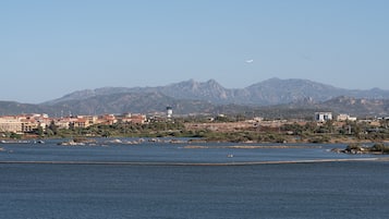 A coastal cityscape with a prominent mountain range in the background, a body of water in the foreground, and a clear sky.