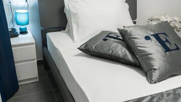 Una cama bien hecha con almohadas blancas y grises, una mesita de noche con una lámpara y un enchufe.