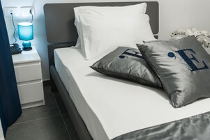 Una cama bien hecha con almohadas blancas y grises, una mesita de noche con una lámpara y un enchufe.