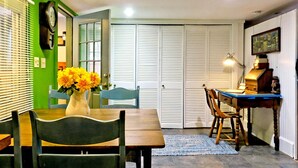 A dining area with a wooden table, chairs, a vase with flowers, a clock, and a closed door with louvered panels. - FARM-TO-TABLE eating, good hot tub soak, S'mores around fire pit, seasonal POOL! (Pownal)