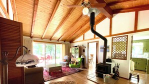 A spacious living room with a high ceiling, wooden beams, a fireplace, and a view through the glass doors.