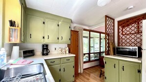 A kitchen with green cabinets, a microwave, a coffee maker, and a window with a view of the outdoors.