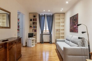 A modern living room with a wooden cabinet, a grey sofa, a TV on a white stand, and bookshelves. - Terrace In The Heart Of City Centre - Wifi, Airconditioning, Washer, Dishawasher (Roma)