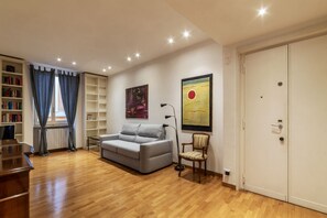 A living room with a grey sofa, a wooden floor, a bookshelf, a radiator, and a door. - Terrace In The Heart Of City Centre - Wifi, Airconditioning, Washer, Dishawasher (Roma)