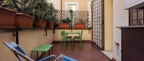 A small outdoor patio with a blue lounge chair, a green table, and potted plants.