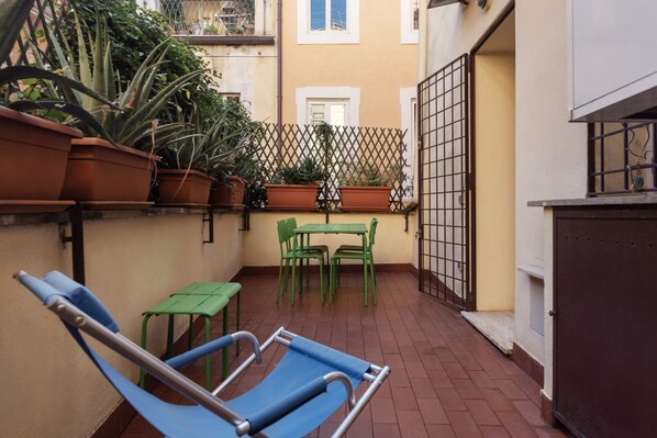 A small outdoor patio with a blue lounge chair, a green table, and potted plants.