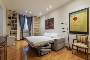 A bedroom with a bed, bedside table, bookshelf, and a large painting on the wall.