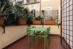A small outdoor patio with a green metal table and chairs, surrounded by potted plants and a lattice fence.