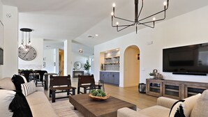 Ein geräumiges Wohnzimmer mit großem Flachbildfernseher, einem Holztisch und einem modernen Kronleuchter.