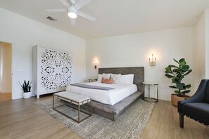 A modern bedroom with a large bed, a bench, a chair, a decorative screen, and a potted plant. - Delaware Estate - Incredible Estate with an acre of resort style amenities and endless activities! (Palm Desert)
