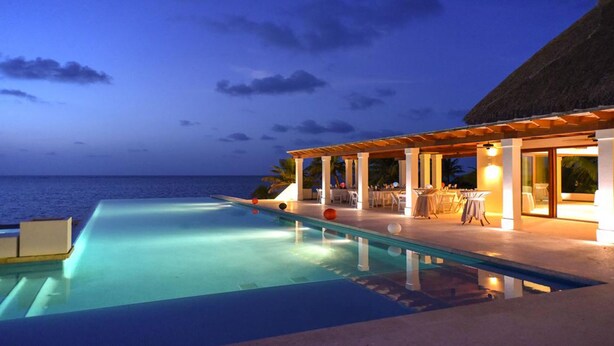 Un espace aménagé au bord de la piscine, offrant une vue sur l’océan au crépuscule.