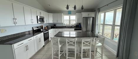 A modern kitchen with white cabinetry, granite countertops, stainless steel appliances, and a large island with bar stools.
