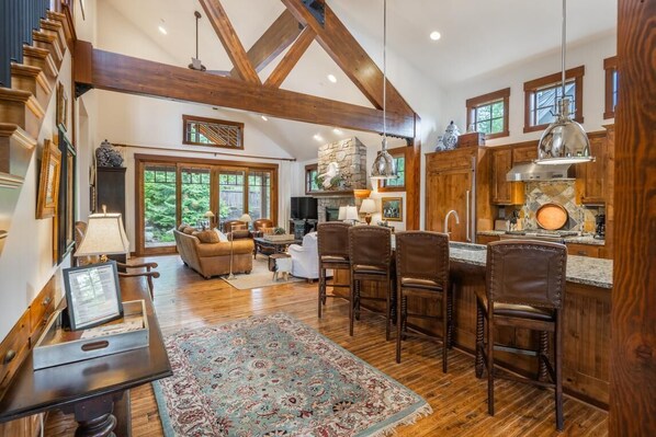 A spacious living room with a fireplace, wooden beams, and a large window overlooking a garden. - Central Location w/ Suncadia Pool Access (Cle Elum)