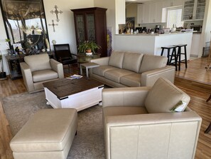 Un salon avec un canapé d’angle beige, une table basse et un coin repas, la cuisine étant visible au fond.