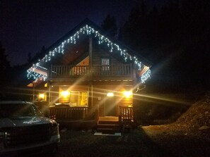 A cabin with a wooden exterior, a balcony, and string lights.