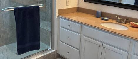 A bathroom with a glass shower, a sink with a mirror above it, and a towel rack.