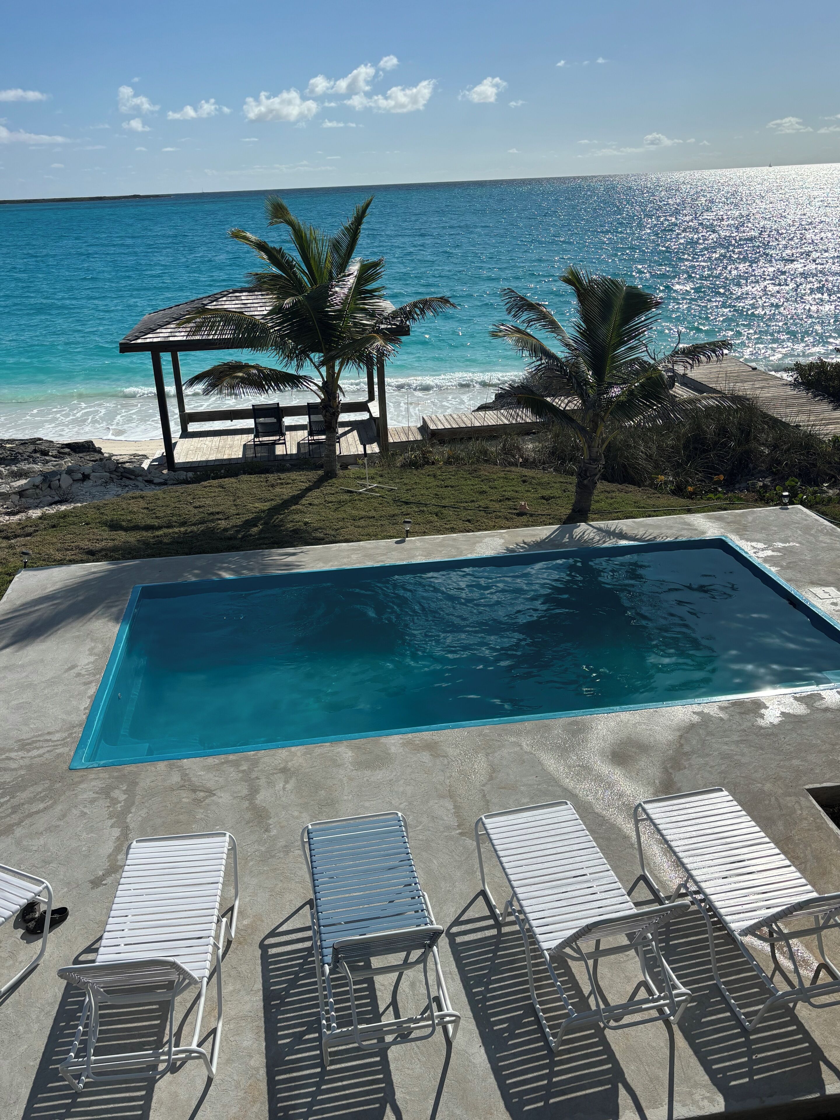 A pool area with lounge chairs, a small pavilion, and a view of the ocean.