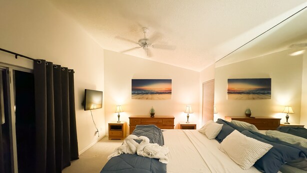 Een slaapkamer met een bed, twee nachtkastjes, een plafondventilator en twee wandlampen.