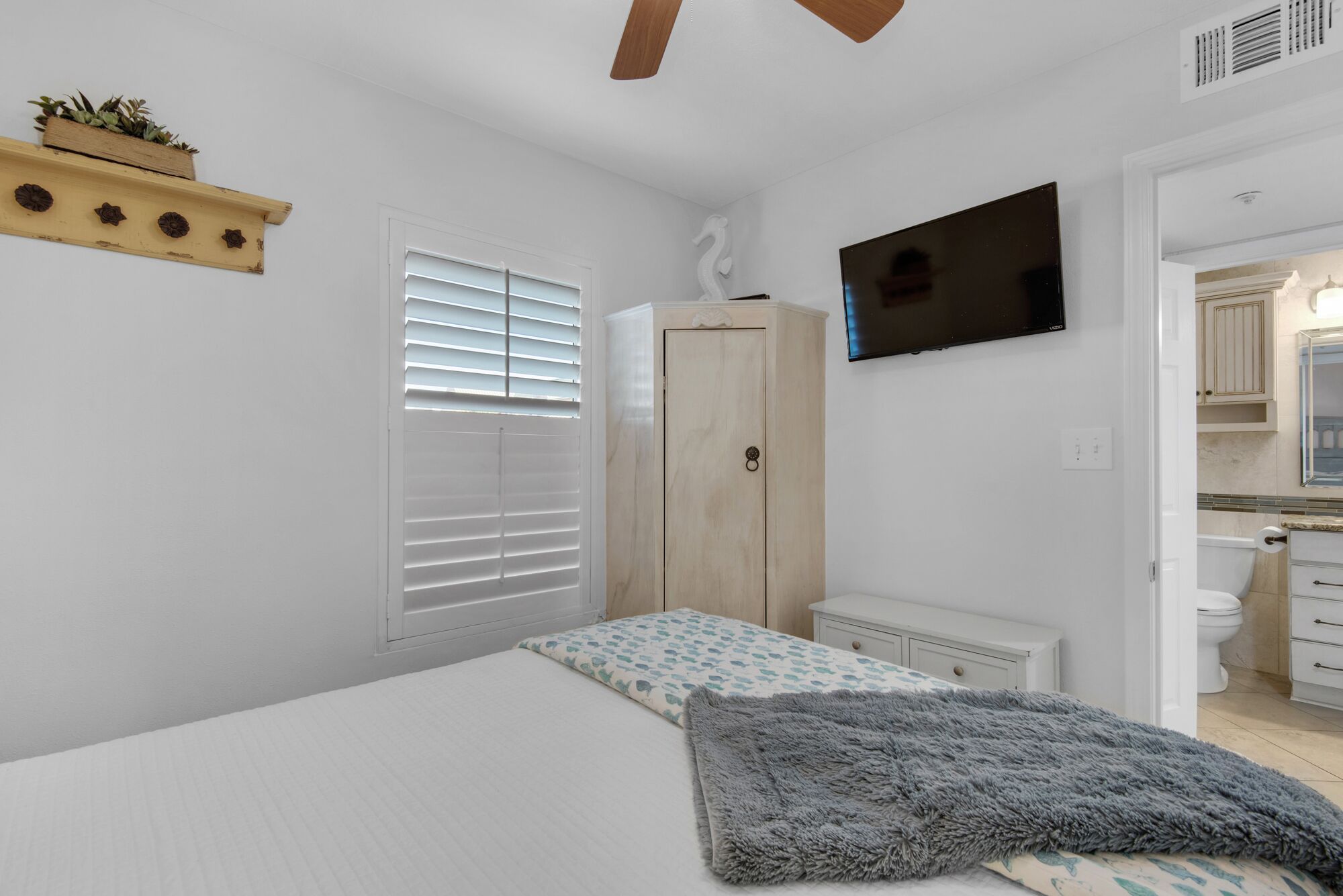 Une chambre à coucher avec un lit, une télévision, une armoire et une salle de bain visible à travers une porte ouverte.