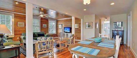A spacious living area with a wooden floor, a dining table with chairs, a television, and a fireplace.