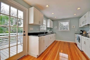 A modern kitchen with white cabinets, a black countertop, and wooden flooring. - Bright & Charming; Close to Beach and Restaurants (Folly Beach)