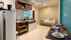 A compact kitchen with a microwave, coffee maker, and storage shelves. A dining area with a table set for two is visible. - Apart Hotel Bella Vida Suites e Apartamentos (Cairu)