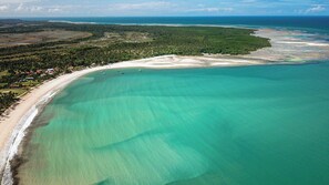 An aerial view of a coastal area with a sandy beach, clear turquoise waters, and a dense forested area. - Apart Hotel Bella Vida Suites e Apartamentos (Cairu)