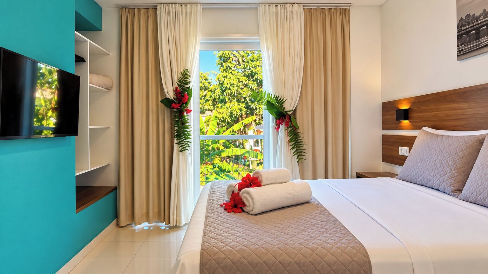 Quarto de hotel com cama, televisão, janela com cortinas e vista para o verde lá fora.