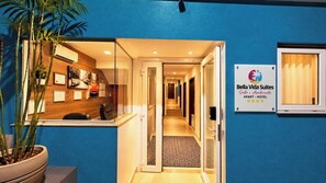 Zona de recepción de un hotel con mostrador de recepción, una planta en maceta y un cartel que indica el nombre y tipo de alojamiento.