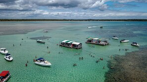 A tropical beach with clear turquoise waters, several boats, and people swimming and enjoying the beach. - Apart Hotel Bella Vida Suites e Apartamentos (Cairu)