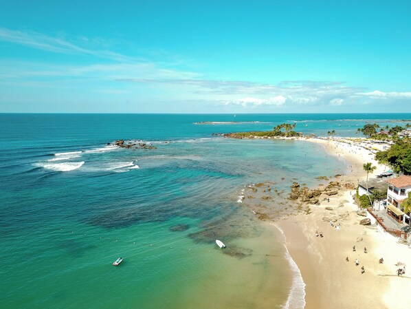 A coastal beach with clear waters, a sandy shore, and a few buildings. - Apart Hotel Bella Vida Suites e Apartamentos (Cairu)