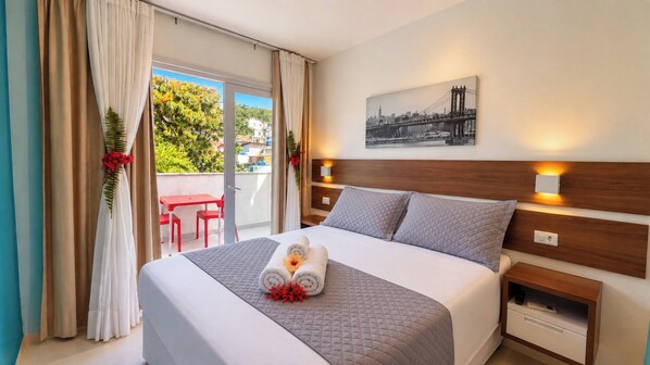 Une chambre d’hôtel avec un lit, une vue sur la ville, un balcon avec des chaises rouges et un tableau au mur.
