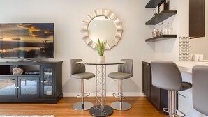 A modern kitchen with a round mirror, two bar stools, a dining table, and a TV on a cabinet. - Modern 1 BR Quiet Condo in Seattle center, pool and fitness, FREE parking (Seattle)